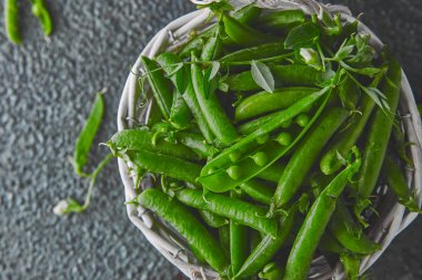 Siyah arka planda taze yeşil bezelye ile beyaz sepet. Vegan ve vejetaryen gıda konsepti. Düz yatma.