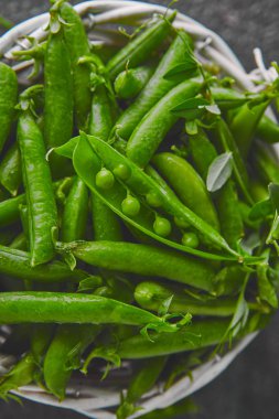 Siyah arka planda taze yeşil bezelye ile beyaz sepet. Vegan ve vejetaryen gıda konsepti. Düz yatma.