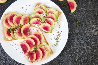 Sağlıklı Kahvaltı, beyaz plaka siyah arka planda dilimlenmiş karpuz turp veya Çin Daikon, Chia ve süzme peynir tost. Üst görünüm. Düz yatıyordu. Boşluk Kopyala. 