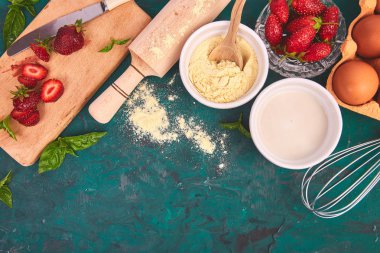 Fırın arka planı. Çilekli turta tarifi. Yeşil arka planda çilekli pasta veya kek pişirmek için çiğ malzemeler. Üst görünüm, düz yatıyordu. Kopyalama alanı. 