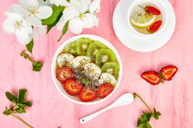 Pembe arka planda çilek, muz, kivi ve chia tohumu ile sağlıklı kahvaltı kase yüzlü. Sağlıklı vegan gıda konsepti