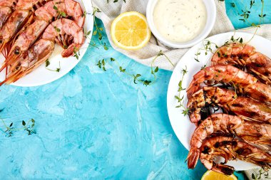 Izgara büyük kaplan karidesler, mavi arka planda, üst görünüm üzerinde baharat, limon, taze otlar ile beyaz plaka üzerinde karides. Izgara deniz ürünleri. Barbekü karidesleri. Boşluk Kopyala.