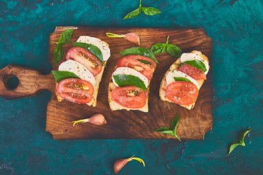Caprese bruschetta kesme tahtası üzerinde tost. Bruschetta domates, mozzarella peyniri ve fesleğen yeşil bir arka plan üzerinde. Geleneksel İtalyan meze veya aperatif, antipasto