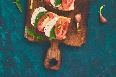 Caprese bruschetta kesme tahtası üzerinde tost. Bruschetta domates, mozzarella peyniri ve fesleğen yeşil bir arka plan üzerinde. Geleneksel İtalyan meze veya aperatif, antipasto