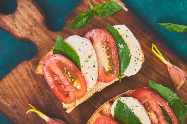 Caprese bruschetta kesme tahtası üzerinde tost. Bruschetta domates, mozzarella peyniri ve fesleğen yeşil bir arka plan üzerinde. Geleneksel İtalyan meze veya aperatif, antipasto