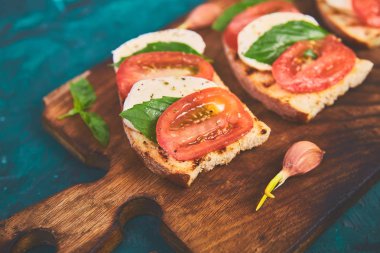 Caprese bruschetta kesme tahtası üzerinde tost. Bruschetta domates, mozzarella peyniri ve fesleğen yeşil bir arka plan üzerinde. Geleneksel İtalyan meze veya aperatif, antipasto