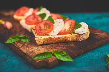 Caprese bruschetta kesme tahtası üzerinde tost. Bruschetta domates, mozzarella peyniri ve fesleğen yeşil bir arka plan üzerinde. Geleneksel İtalyan meze veya aperatif, antipasto