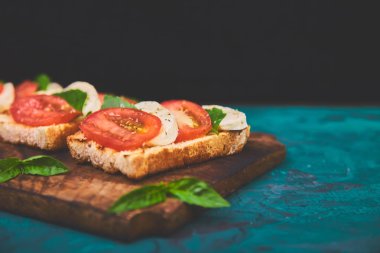 Caprese bruschetta kesme tahtası üzerinde tost. Bruschetta domates, mozzarella peyniri ve fesleğen yeşil bir arka plan üzerinde. Geleneksel İtalyan meze veya aperatif, antipasto