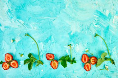 Mavi bir arka plan üzerinde çilek ile Düz yatıyordu kompozisyon. Çilek ve yapraklardan yapılmış renkli parlak desen. Meyve çerçevesi. Yaz konsepti. Düz yatıyordu, üstten bak. Kopyalama alanı.