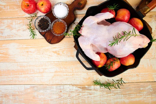Whole raw chicken in skillet  or iron pan with rosemary leaf, thyme, lemon, red apples . Ready to cook. Cooking background. Copy space