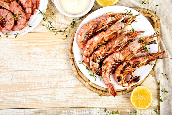 Grilled big tiger shrimps prawns on white plate with spices, lemon, fresh herbs on white wooden background, top view. Grilled seafood. Barbecue shrimps. Copy space.