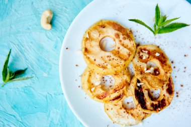 Mavi arka plan üzerinde beyaz plaka üzerinde cinamon ile ızgara elma.