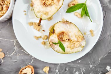 Lezzetli armutlar, ballı ve fındıklar, gri arka plan masasında beyaz tabakta. Üst Manzara. Düz yatıyordu. Boşluğu kopyala.