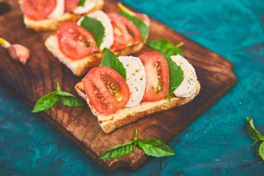 Caprese bruschetta kesme tahtası üzerinde tost. Bruschetta domates, mozzarella peyniri ve fesleğen yeşil bir arka plan üzerinde. Geleneksel İtalyan meze veya aperatif, antipasto