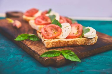 Caprese bruschetta kesme tahtası üzerinde tost. Bruschetta domates, mozzarella peyniri ve fesleğen yeşil bir arka plan üzerinde. Geleneksel İtalyan meze veya aperatif, antipasto