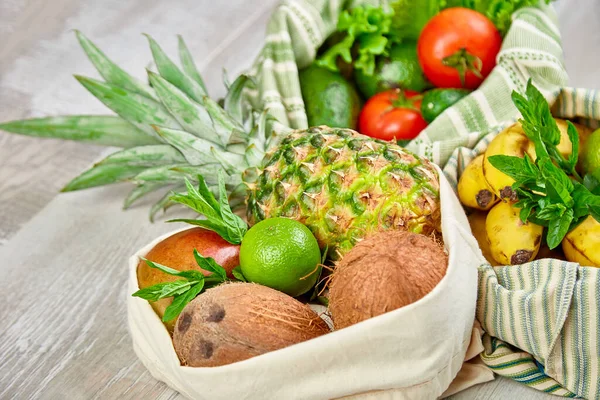 Fresh vegetables and fruits in eco cotton bags on table in the kitchen. Flat lay, top view. Zero waste, plastic free lifestyle concept. Healthy veggie food diet and detox.