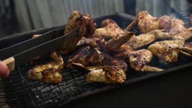 Mangal ve açık havada ızgara yapılan tavuk kanatları için metal maşa kullanan adam, mangal ızgarasında kızartılan et, arka bahçede pişirilen aşçı..