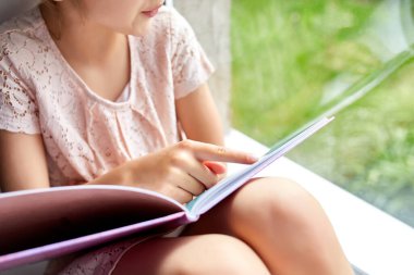 Evde, pencere kenarında kitap okuyan sevimli küçük bir kız evde ders çalışan bir çocuk, karantina, evde kalmak, yaşam tarzı....