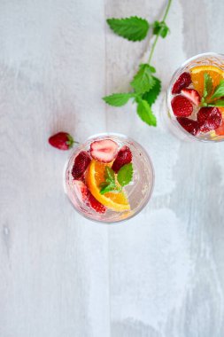 Çilekli, portakallı ve nane şekerli yaz kokteyli beyaz masada, ev yapımı ferahlatıcı limonata, çilekli punç, üst manzara, kopyalama alanı..