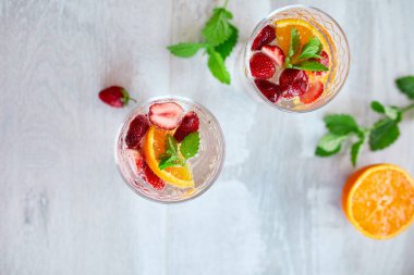 Çilekli, portakallı ve nane şekerli yaz kokteyli beyaz masada, ev yapımı ferahlatıcı limonata, çilekli punç, üst manzara, kopyalama alanı..