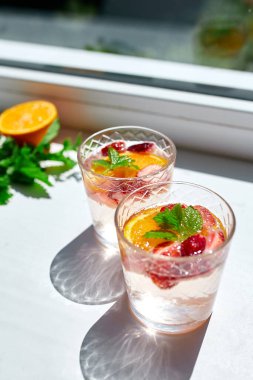 Ev yapımı ferahlatıcı limonata, çilekli, portakallı ve naneli kokteyl beyaz masada sert güneş ışığı çilekli punç, kopyalama alanı.