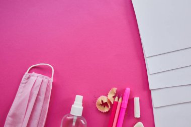Koronavirüs salgınından sonra okula yeni bir gerçeklikle dönmek, okul gereçleri, koruyucu maske ve antiseptik pembe arka planda.