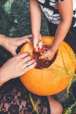 Kadın ve çocuk elleri Cadılar Bayramı için oymadan önce balkabağından tohum ve lifli malzemeler çıkarır. Jack-o-fener. Tonlu fotoğraf. Kızı ve annesi.