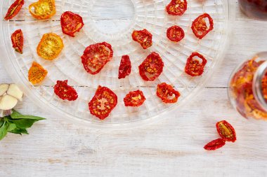 Beyaz ahşap arka planda kurutucudan süzgeçte kurutulmuş otlarla ev yapımı kurutulmuş domatesler. Üst görünüm, kopyalama alanı, düz uzanma