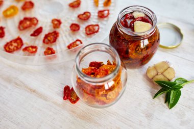 Ev yapımı güneşte kurutulmuş domatesler, beyaz ahşap zemin üzerinde cam bir kavanozda zeytinyağında sarımsak. Üst Manzara. Mutfak için yazdır