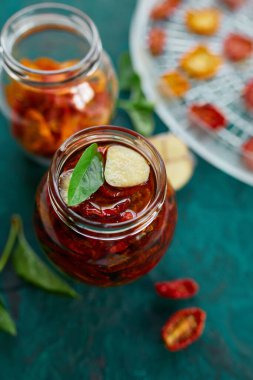 Ev yapımı güneşte kurutulmuş domatesler, zeytinyağında sarımsak koyu yeşil arka planda cam bir kavanozda. Üst Manzara. Mutfak için yazdır