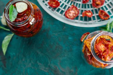 Ev yapımı güneşte kurutulmuş domatesler, zeytinyağında sarımsak koyu yeşil arka planda cam bir kavanozda. Üst Manzara. Mutfak için yazdır