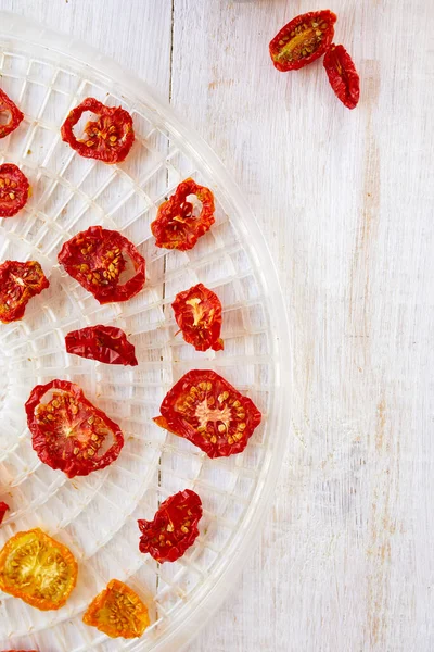 Beyaz ahşap arka planda kurutucudan süzgeçte kurutulmuş otlarla ev yapımı kurutulmuş domatesler. Üst görünüm, kopyalama alanı, düz uzanma