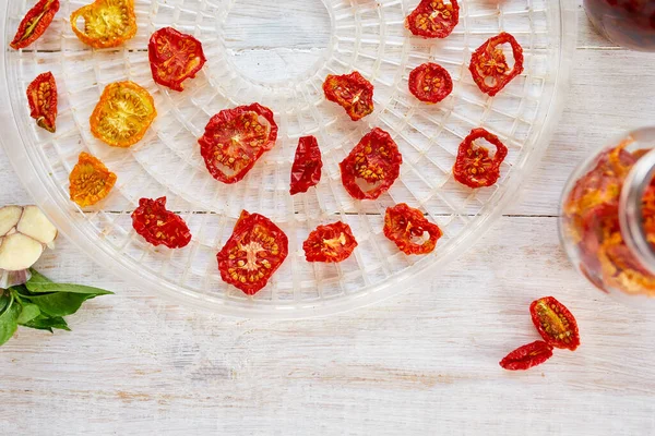 Beyaz ahşap arka planda kurutucudan süzgeçte kurutulmuş otlarla ev yapımı kurutulmuş domatesler. Üst görünüm, kopyalama alanı, düz uzanma