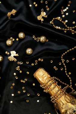 İçinde konfeti yıldızları ve şenlikli siyah arka planda parti flamaları olan altın şampanya şişesi. Noel, doğum günü ya da düğün konsepti. Düz yatıyordu.