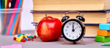 Okul gereçlerinin bayrağı. Yeşil arka planda kitaplar ve kırmızı elma. Çalar saatle hayat devam ediyor. Boşluğu kopyala.