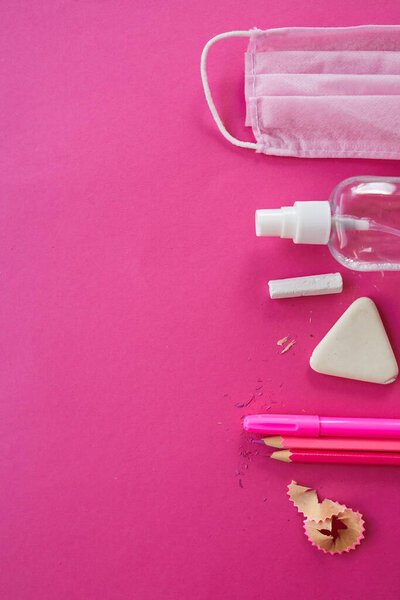 Flat lay schooling after the coronavirus pandemic, Back to school in a new reality, School supplies, protective mask and antiseptic on a pink background, space for text