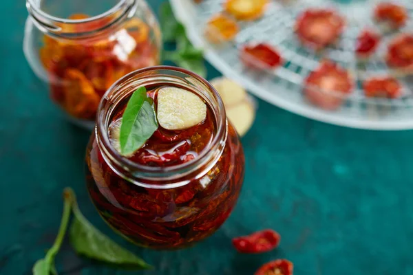 Ev yapımı güneşte kurutulmuş domatesler, zeytinyağında sarımsak koyu yeşil arka planda cam bir kavanozda. Üst Manzara. Mutfak için yazdır