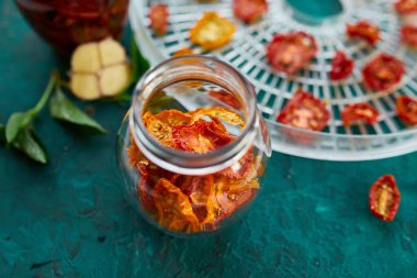 Ev yapımı güneşte kurutulmuş domatesler, zeytinyağında sarımsak koyu yeşil arka planda cam bir kavanozda. Uzayı kopyala, kapat. Mutfak için yazdır