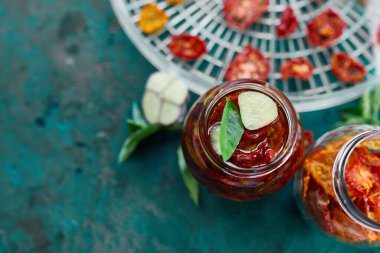 Ev yapımı güneşte kurutulmuş domatesler, zeytinyağında sarımsak koyu yeşil arka planda cam bir kavanozda. Üst Manzara. Mutfak için yazdır