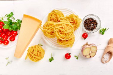 Makarna pişirmek için gerekli malzemeler - tagliatelle, domates, sarımsak, fesleğen, parmesan peyniri beyaz ahşap arka plan düzlüğü, üst görünüm, çerçeve, kopyalama alanı, İtalyan gıda kavramı.