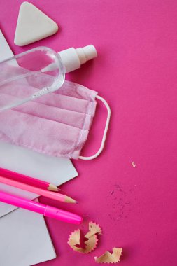 Koronavirüs salgınından sonra okula yeni bir gerçeklikle dönmek, okul gereçleri, koruyucu maske ve antiseptik pembe arka planda.