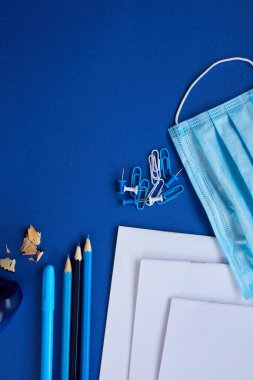 Coronavirüs salgınından sonra okula yeni bir gerçeklikle dönmek, okul gereçleri, koruyucu maske ve antiseptik mavi arka planda, mesaj için yer