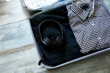 Evde sıradan erkek eşyalarıyla bavul hazırlamak. Kotlar, gömlekler, kulaklıklar seyahat, seyahat, tatil için bavullar. Boşluğu kopyala.