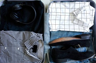 Evde sıradan erkek eşyalarıyla bavul hazırlamak. Kotlar, gömlekler, kulaklıklar seyahat, seyahat, tatil için bavullar. Boşluğu kopyala.