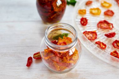 Ev yapımı güneşte kurutulmuş domatesler, beyaz ahşap zemin üzerinde cam bir kavanozda zeytinyağında sarımsak. Uzayı kopyala, kapat. Mutfak için yazdır.