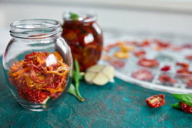 Ev yapımı güneşte kurutulmuş domatesler, zeytinyağında sarımsak koyu yeşil arka planda cam bir kavanozda. Uzayı kopyala, kapat. Mutfak için yazdır