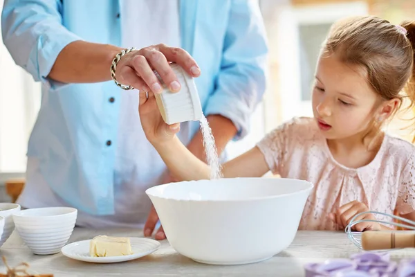 Father and daughter preparing dough together in kitchen, adding sugar to bowl while cooking pastry at home, Family cooking at home, fatherhood and family weekend concept.