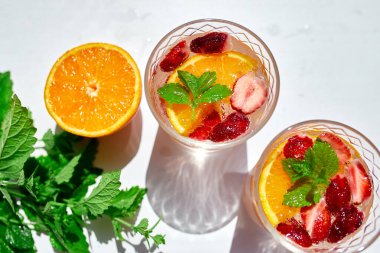 Ev yapımı ferahlatıcı limonata, çilekli, portakallı ve nane şekerli kokteyl beyaz masada sert güneş ışığı çilekli punç, üst manzara, kopyalama alanı.