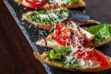 Mozzarella peyniri, domates, pesto sos ve parmesan peyniri, siyah bir taş, ahşap bir masa ile İtalyan bruschettes. Kopya alanı, seçici odak