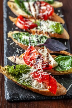 Mozzarella peyniri, domates, pesto sos ve parmesan peyniri, siyah bir taş, ahşap bir masa ile İtalyan bruschettes. Kopya alanı, seçici odak
